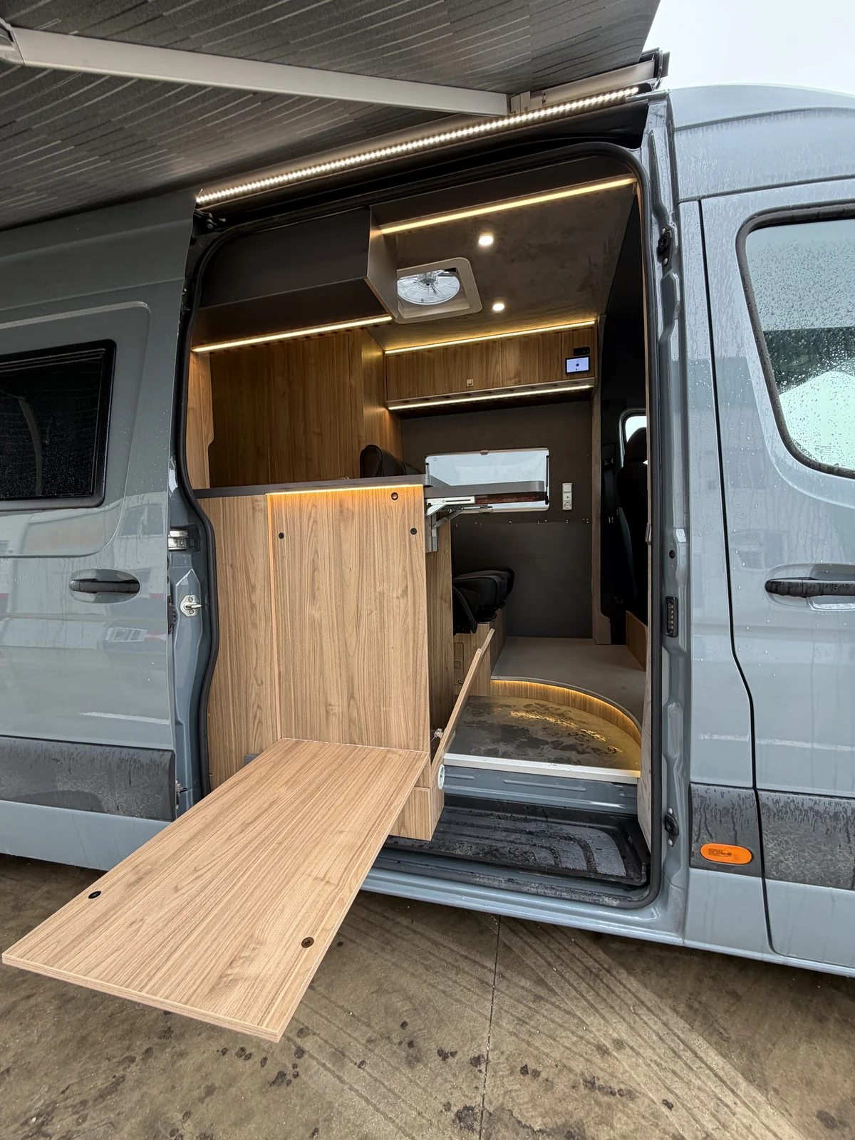 Fold-out exterior table beside the illuminated entrance of a BeBrightCamp campervan