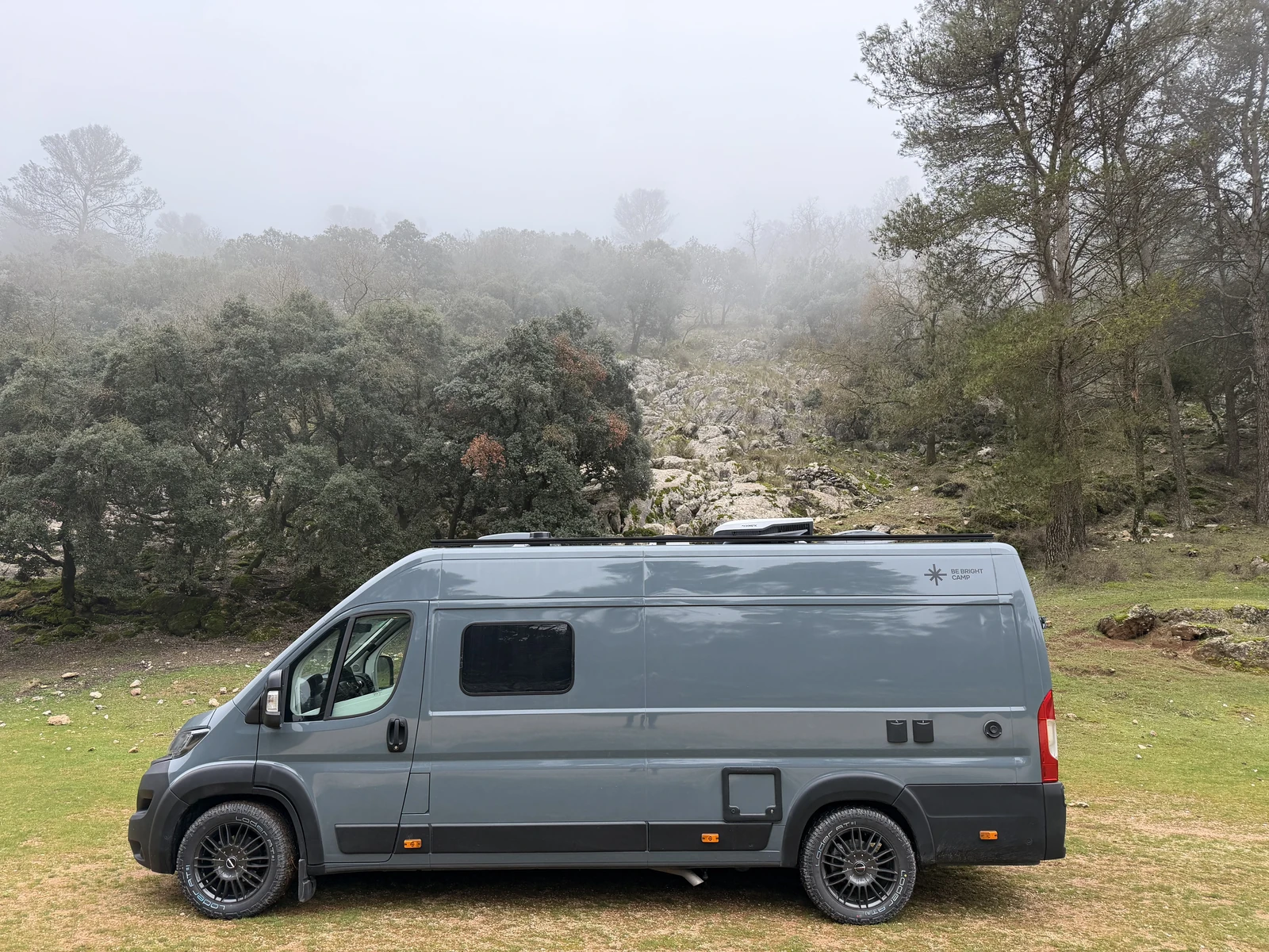 Grey BeBrightCamp campervan parked beside a misty wooded hillside
